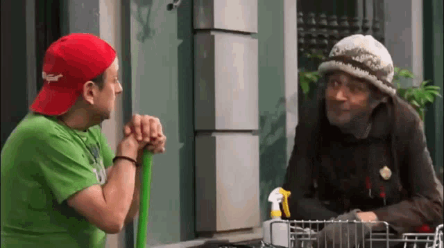 a man wearing a red budweiser hat talks to another man in a green shirt