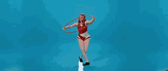 a woman in a red top and shorts is holding a hula hoop in her hands .