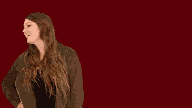 a woman with long hair is standing in front of a red background and making a funny face .