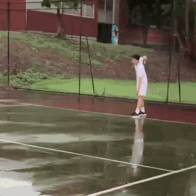 a person playing tennis in the rain with a fence in the background