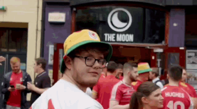 a man wearing a hat and glasses stands in front of a store called the moon