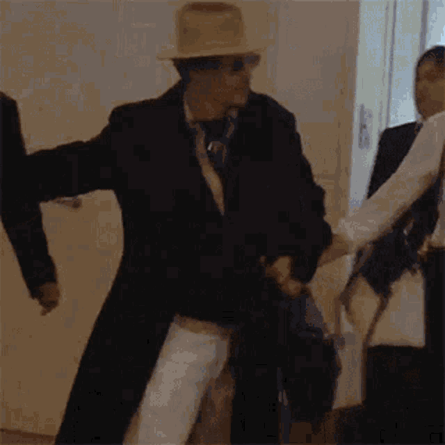 a man wearing a hat and sunglasses is dancing in a hallway while holding a bag .