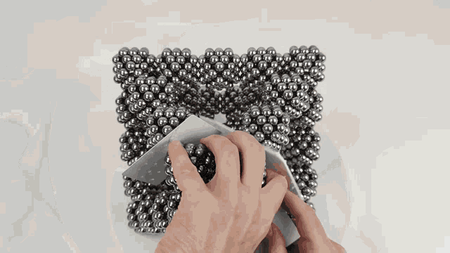 a person is holding a piece of paper in front of a pile of metal beads