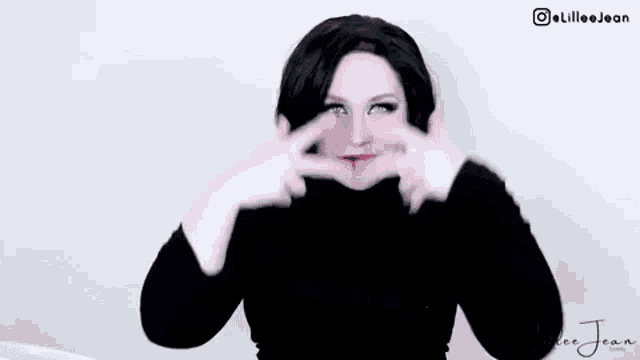 a woman is wearing a black turtleneck and making a funny face while holding her hands to her chest .