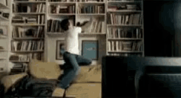 a man is jumping in the air while sitting on a couch in a living room .