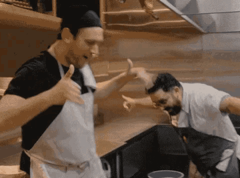 two men in aprons are giving each other a high five in a kitchen