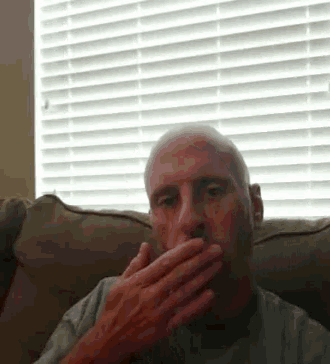 a man is sitting on a couch covering his mouth with his hand