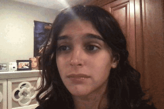 a woman 's face is shown with a picture of a man on the wall in the background