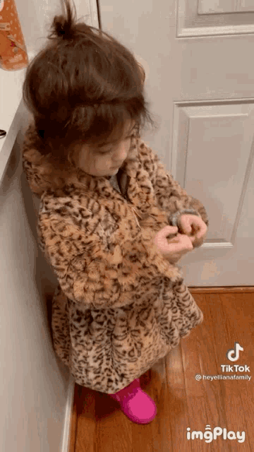 a little girl wearing a leopard print coat and pink shoes is standing in front of a door