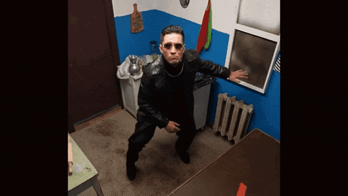 a man in a black leather jacket and sunglasses is standing in a kitchen