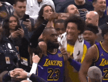 a basketball player wearing a purple lakers jersey is surrounded by fans