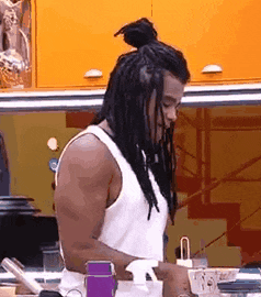 a man with dreadlocks is standing in a kitchen with a bun on his head .