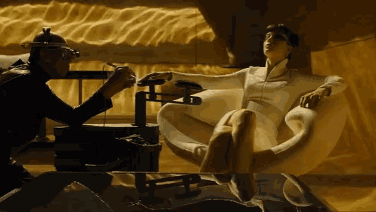 a man is standing next to a woman who is sitting in a chair