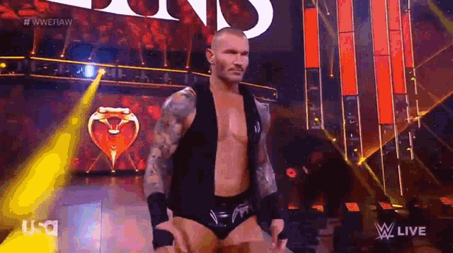 a wrestler is standing on a stage with his hands in his pockets and looking at the camera .