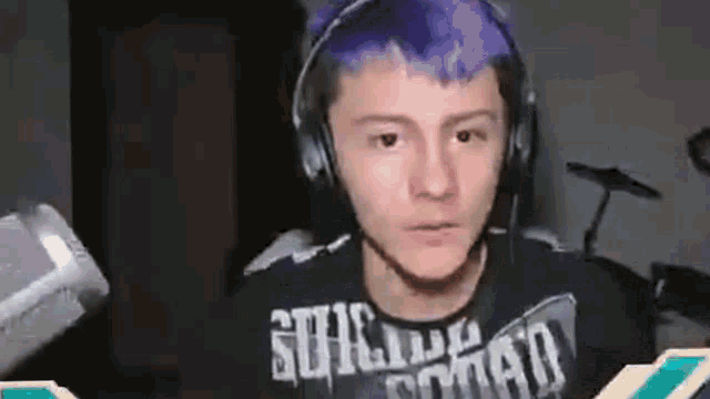 a young man with purple hair wearing headphones and a suicide squad shirt .
