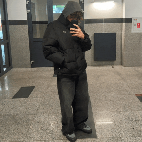 a person taking a selfie in a hallway with a hood on