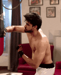 a shirtless man is hitting a punching bag with his fist in a living room
