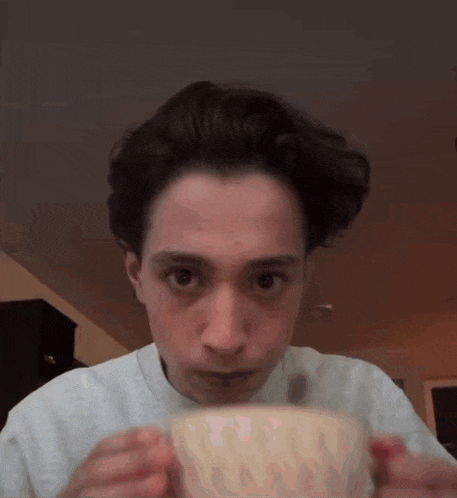 a young man is drinking from a white cup .