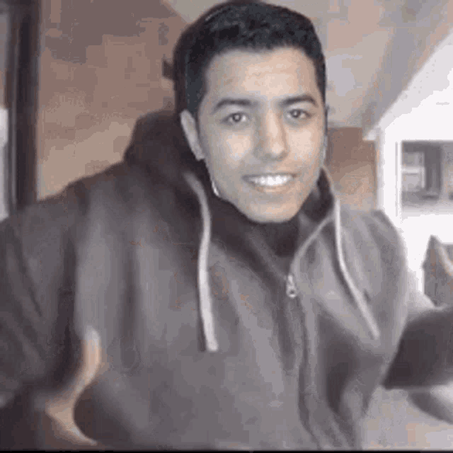 a man wearing a hoodie is smiling and holding a cell phone .