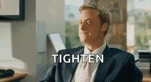 a man in a suit and tie is sitting at a desk with the word tighten written on his face .