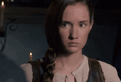 a woman in a braided ponytail looks at the camera with a candle in the background