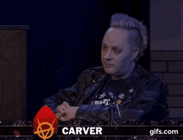 a man with a mohawk is sitting in front of a microphone and saying `` for fuck 's sake ... ''