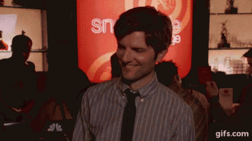 a man in a striped shirt and tie is smiling in front of a sign that says sn on it