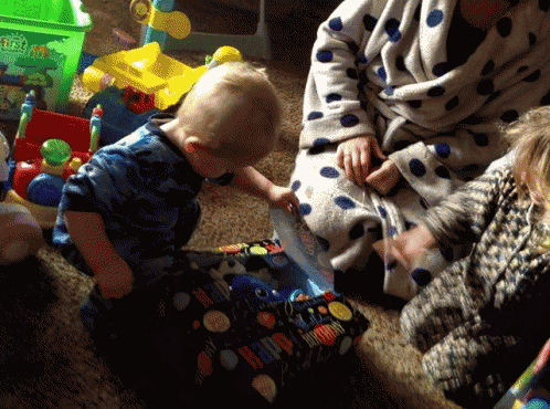 a woman in a polka dot robe sits on a couch with two children playing with toys