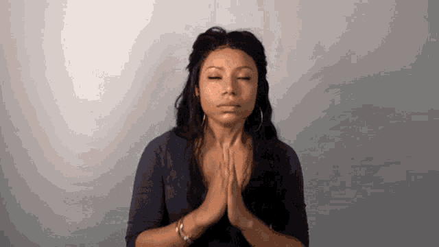 a woman is praying with her eyes closed and her hands together .