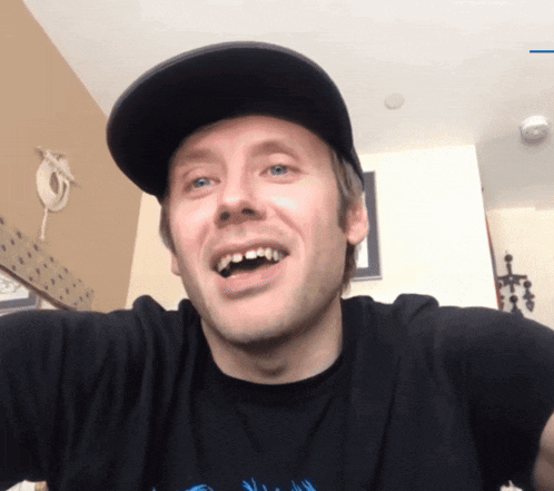 a man wearing a hat and a black shirt is smiling with his mouth open