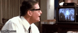 a man wearing glasses is sitting in front of a television and laughing .