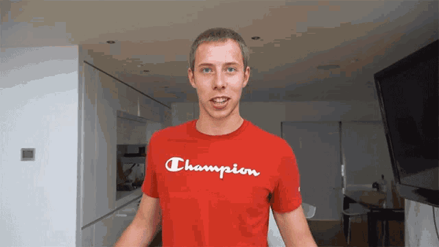 a man wearing a red champion t-shirt stands in a kitchen