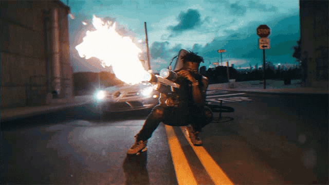 a man is kneeling down in front of a stop sign with a car in the background