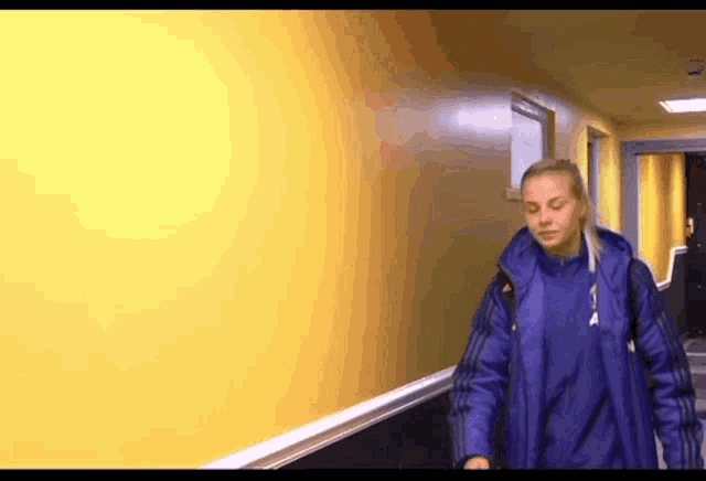 a woman in a blue coat is walking down a hallway .