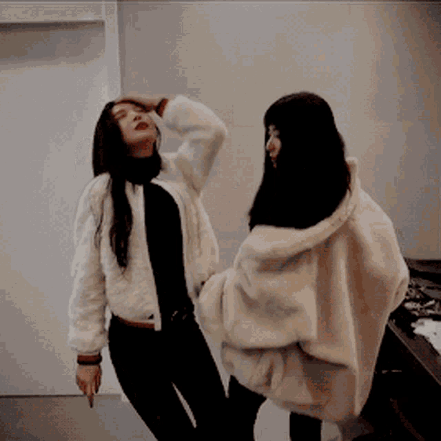 two women are standing next to each other one wearing a white fur coat