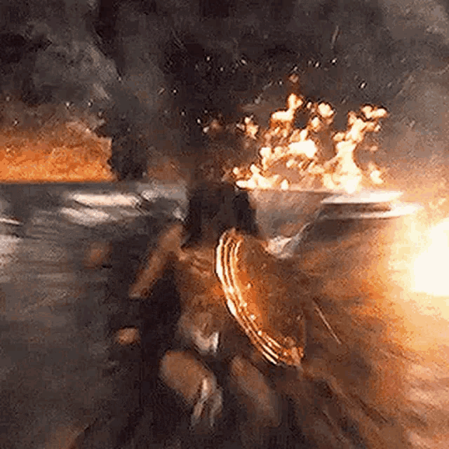 wonder woman is holding a shield in front of a large fire .