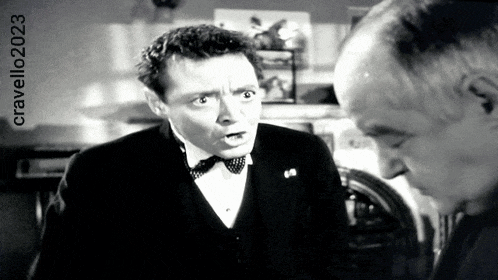 a man in a tuxedo is talking to another man in a black and white photo taken by cravello 2023