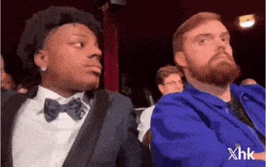 a man with a beard is sitting next to another man in a suit and bow tie