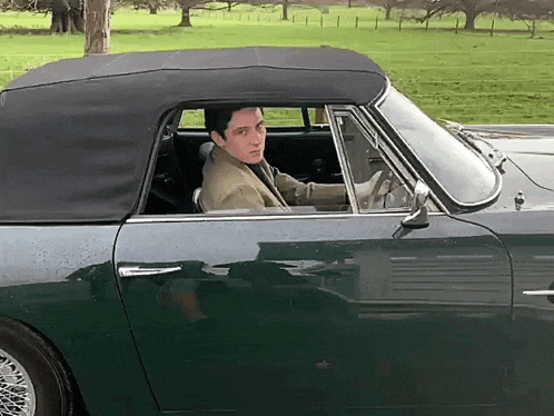 a man is driving a green convertible car with a black top