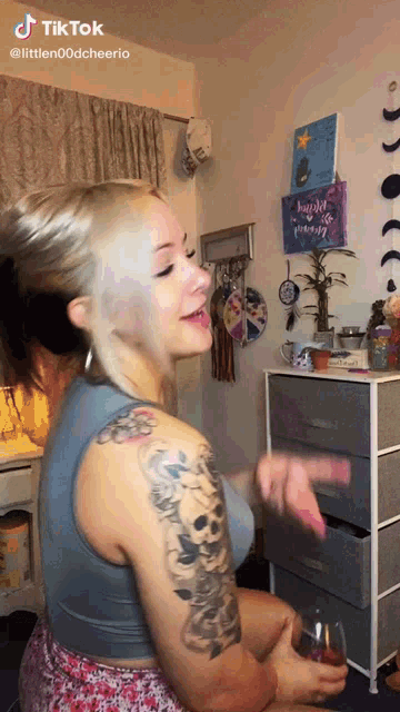 a woman with a tattoo on her arm is sitting in front of a dresser with a sign that says " have a great day "