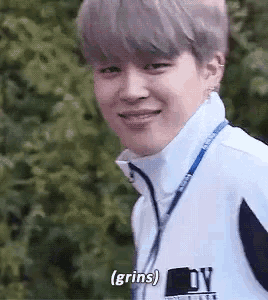 a young man wearing a white jacket with a lanyard around his neck is smiling and saying grins