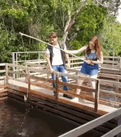 a man and a woman are fishing in a pond on a wooden bridge .