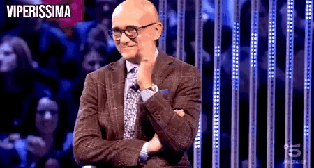 a bald man wearing glasses and a suit is standing in front of a crowd with the words viperissima written on the bottom