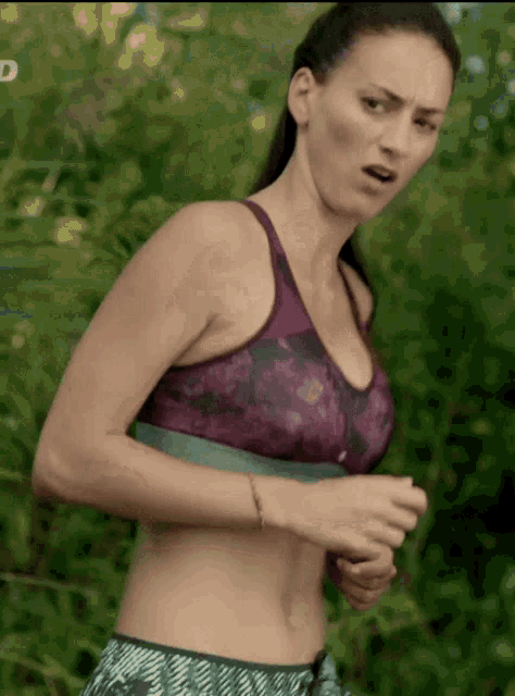 a woman in a purple sports bra is running in the woods with the letter d in the corner