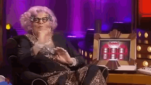 a woman in a pink wig and glasses is sitting in a chair in front of a machine .