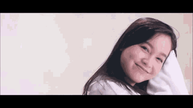 a young girl is smiling and looking at the camera while holding her head .
