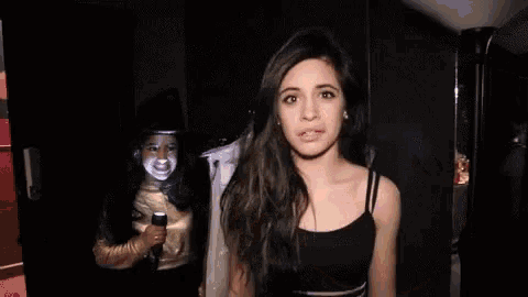 a woman is sticking her tongue out while another woman stands behind her holding a microphone .