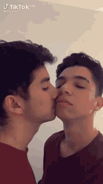 a couple of young men are kissing each other on the nose .