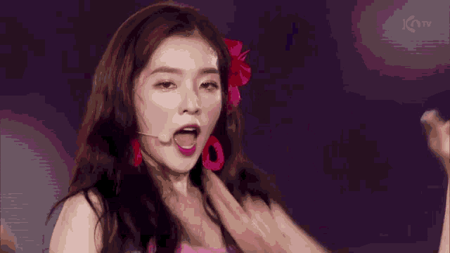 a woman in a pink dress with a red flower in her hair making a peace sign