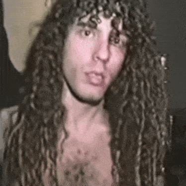 a man with long curly hair is without a shirt and is looking at the camera .
